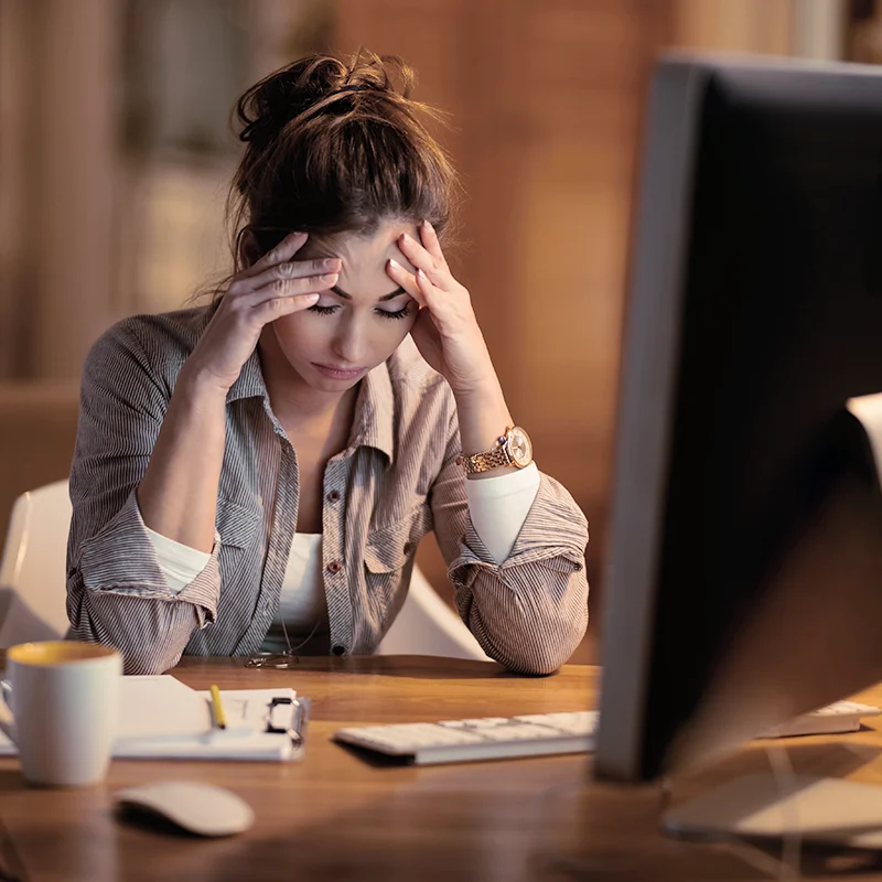 A frustrated business woman sits looking confused at a desk with a computer and tech
